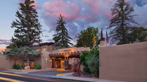 Exterior view of La Posada hotel at dusk, featuring adobe architecture and surrounding trees under a colorful sky.