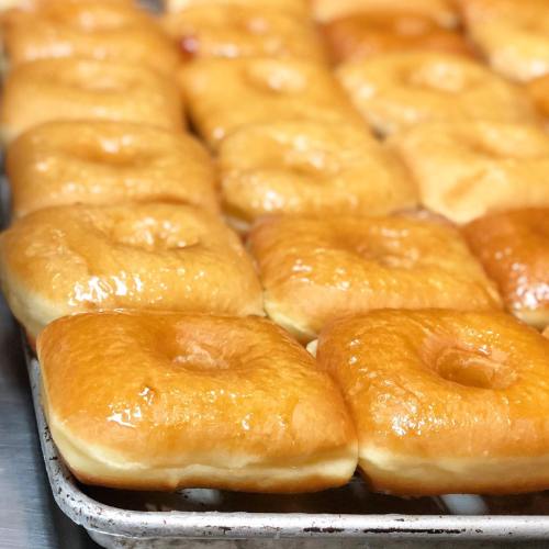 A tray of freshly glazed donuts, golden brown and shiny, arranged in neat rows.