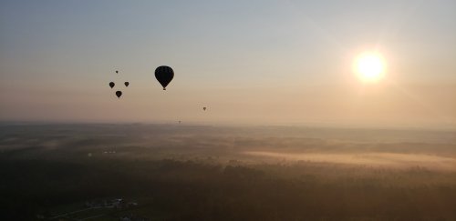 Hot air balloons float above a misty landscape at sunrise, with the sun casting a warm glow over the horizon.