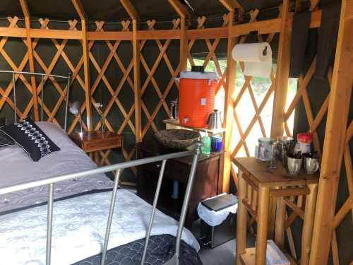 Cozy yurt interior featuring a bed, wooden furniture, and a kitchenette area with a water cooler and supplies.