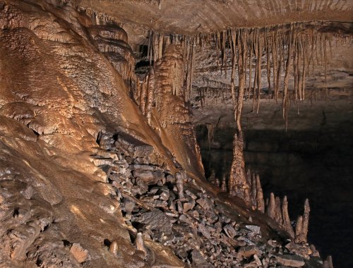 Stalactites and stalagmites in a dimly lit cave, showcasing intricate rock formations and textures.