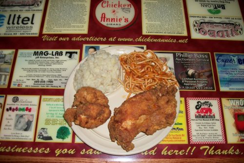 A plate of fried chicken, rice, and spaghetti on a colorful restaurant table.