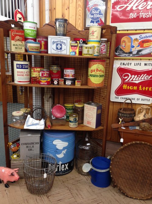 A vintage display shelf filled with various old cans, jars, and kitchen items, showcasing nostalgic collectibles.