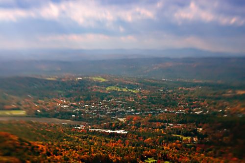 A blurred aerial view of a colorful autumn landscape with trees and a small town nestled in the valley.