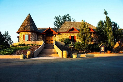 A charming stone house with a conical roof, surrounded by greenery and a landscaped pathway.