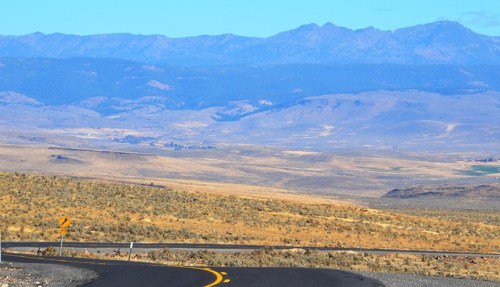 Winding road through a vast, arid landscape with distant mountains under a clear blue sky.