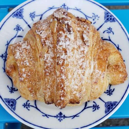 A golden-brown croissant dusted with powdered sugar, placed on a decorative blue and white plate.