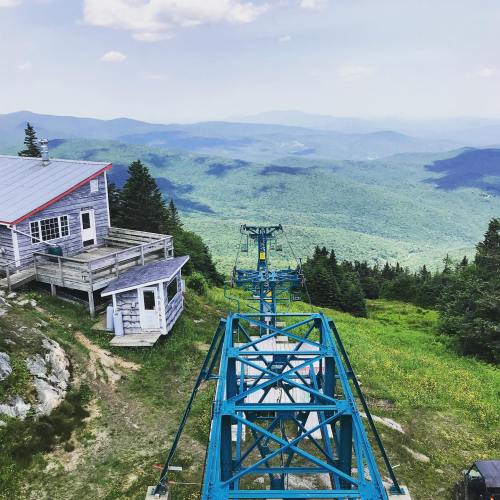 A scenic view from a mountaintop, featuring a ski lift and lush green mountains in the background under a clear sky.