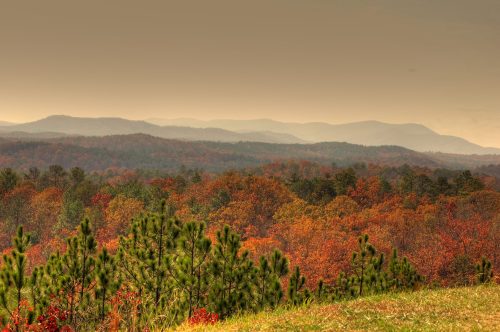 A scenic view of rolling mountains and vibrant autumn foliage under a hazy sky.