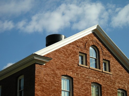 A brick building with a black cylindrical structure on the roof, under a blue sky with scattered clouds.