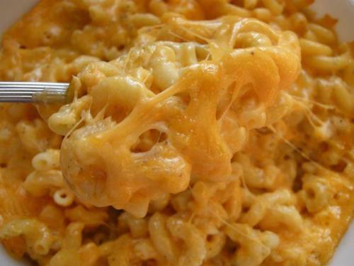 A close-up of cheesy macaroni and cheese, with gooey melted cheese stretching from a spoon.