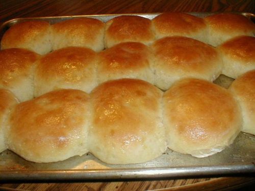 A tray of golden-brown, freshly baked dinner rolls arranged in a neat row.