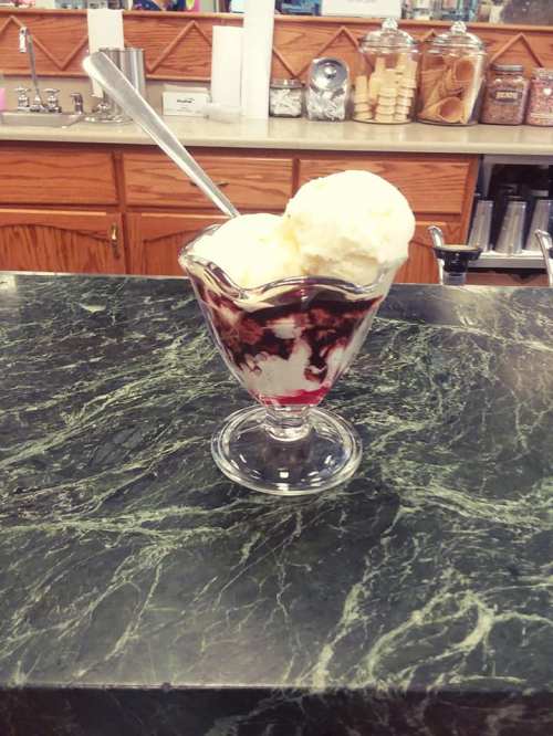 A glass dessert dish filled with ice cream and cherry sauce, sitting on a green marble countertop.