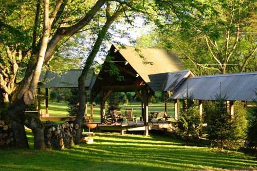 A serene outdoor space with a wooden pavilion, rocking chairs, and lush greenery under a clear sky.