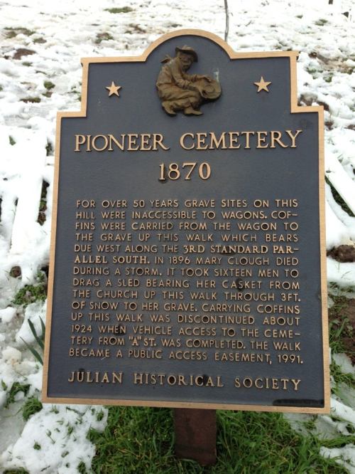 Sign about Pioneer Cemetery, detailing its history and access challenges, with snow-covered ground in the background.
