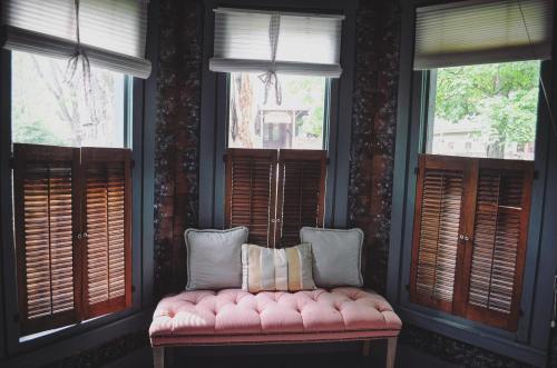 Cozy corner with a pink tufted bench, surrounded by wooden shutters and natural light from the windows.