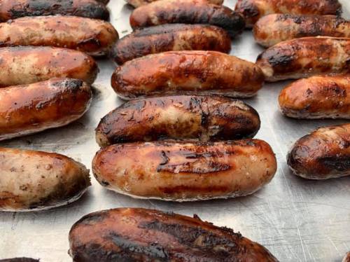 Grilled sausages with a charred exterior, arranged closely on a metal surface.