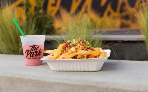 A plate of loaded fries topped with meat and cheese, next to a cup of pink drink, set against a colorful background.