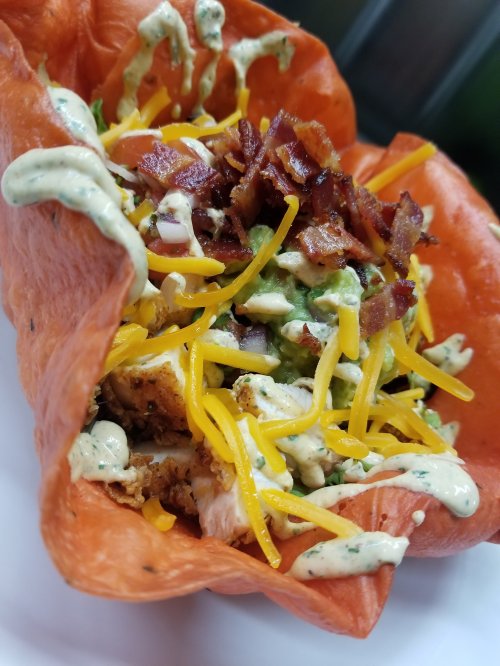 A colorful taco bowl filled with chicken, guacamole, cheese, bacon, and drizzled with a creamy sauce.