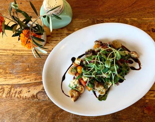 A vibrant salad with greens, cherry tomatoes, croutons, and a drizzle of balsamic glaze, alongside a small flower vase.