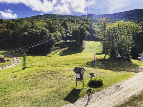 A scenic view of a green hillside with a ski lift, trees, and a signpost under a bright blue sky.