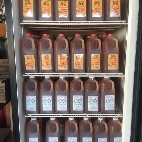 A refrigerator filled with various jugs of apple cider, featuring colorful labels and different sizes.