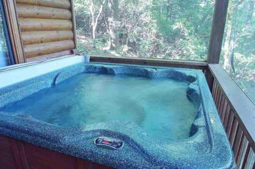 A hot tub on a screened porch, surrounded by trees and nature. Water is calm and inviting.