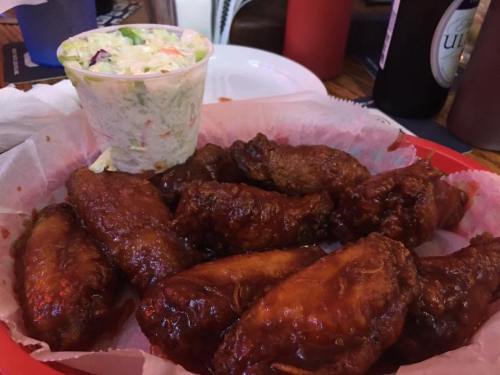 A plate of crispy chicken wings with a side of coleslaw in a cup, served on a red tray.