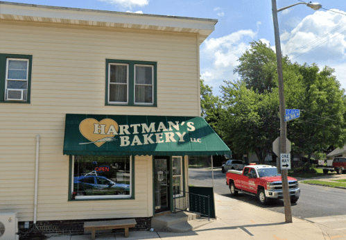 Exterior of Hartman's Bakery with a green awning, open sign, and a red truck parked nearby on a sunny day.