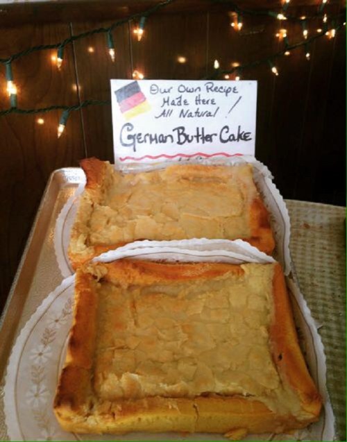 A tray of German butter cake with a sign that reads "Our Own Recipe Made Here All Natural." Festive lights in the background.