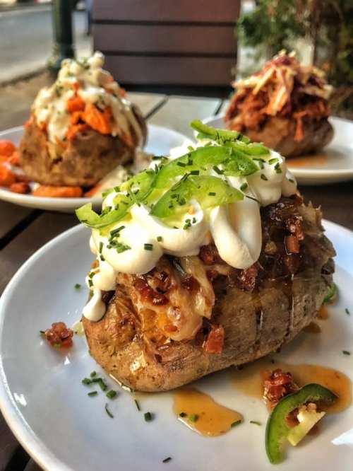 Three loaded baked potatoes topped with various ingredients, including sour cream, green onions, and shredded meat.