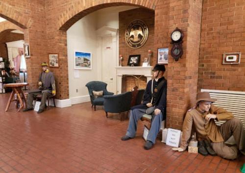 Two life-sized mannequins in historical military uniforms sit in a brick room with a fireplace and various decorations.