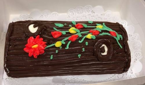 A chocolate log cake decorated with colorful icing flowers and leaves on a white lace doily.