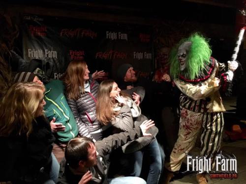 A group of people reacts in surprise to a clown performer at Fright Farm, surrounded by Halloween decorations.