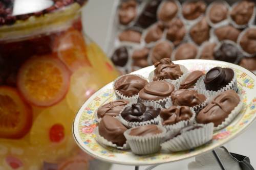 A decorative plate of assorted chocolates in paper cups, with a jar of fruit preserves in the background.