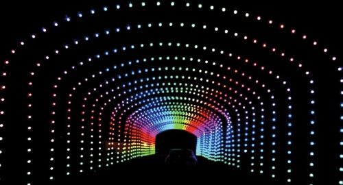 A colorful, illuminated tunnel with vibrant lights creating a rainbow effect against a dark background.