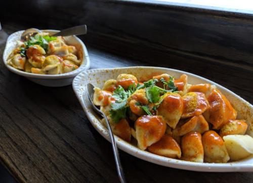 Two bowls of colorful Indian street food, featuring spiced dumplings topped with herbs and sauces, on a wooden table.
