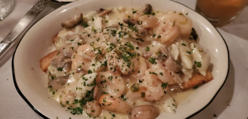 A bowl of shrimp and seafood over toasted bread, topped with creamy sauce and garnished with parsley.