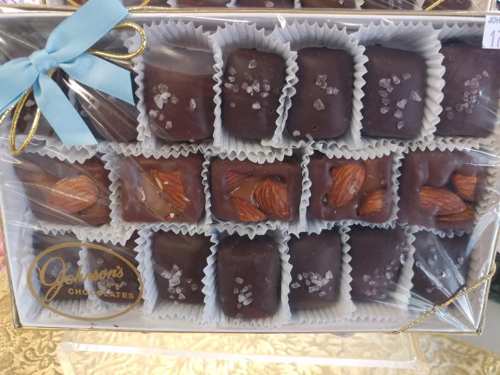 A box of assorted chocolates, some topped with almonds and sea salt, wrapped in clear plastic with a blue ribbon.