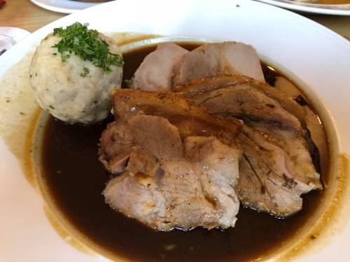 A plate of tender pork slices in rich gravy, accompanied by a round dumpling and garnished with parsley.