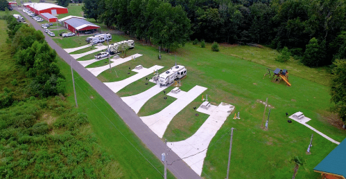 Aerial view of a grassy RV park with several parked RVs and a playground in the background.