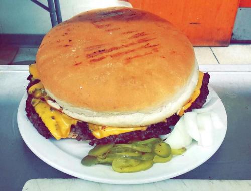 A large burger with melted cheese, pickles, and onions on a plate, featuring a thick, toasted bun.