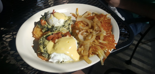 A plate of eggs Benedict with spinach and bacon, served with crispy hash browns and sautéed onions.