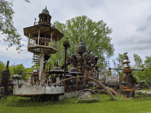A whimsical outdoor sculpture park featuring a treehouse, large metal structures, and lush greenery.