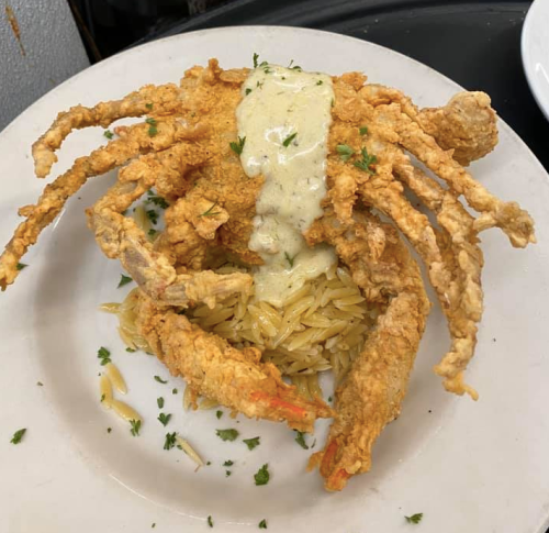 Fried soft-shell crab topped with creamy sauce, served on a bed of orzo pasta, garnished with parsley.