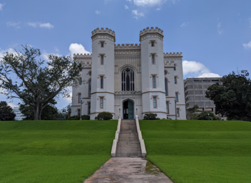 A large, white castle-like building with towers, set on a green lawn under a blue sky.