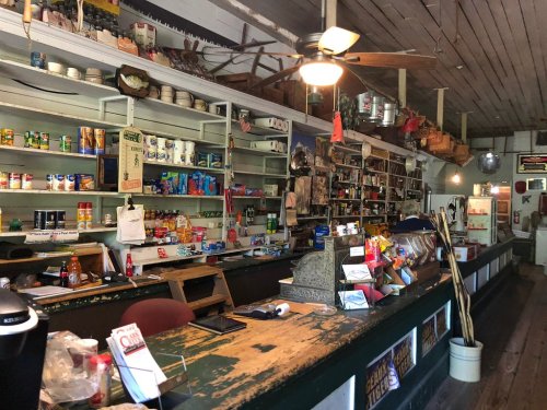 Interior of a vintage general store with shelves stocked with various goods and a wooden counter in the foreground.