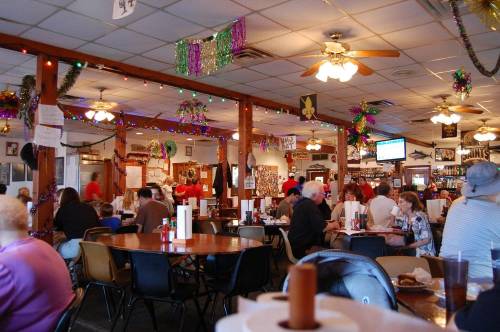 A bustling restaurant interior decorated with festive lights and Mardi Gras decorations, filled with diners at tables.