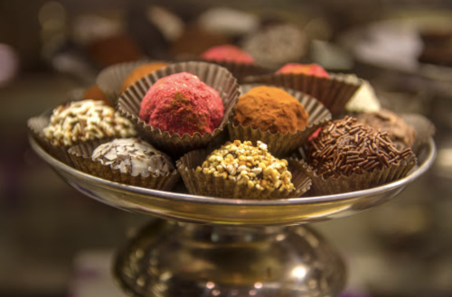 A silver platter holds an assortment of colorful chocolate truffles in decorative paper cups.