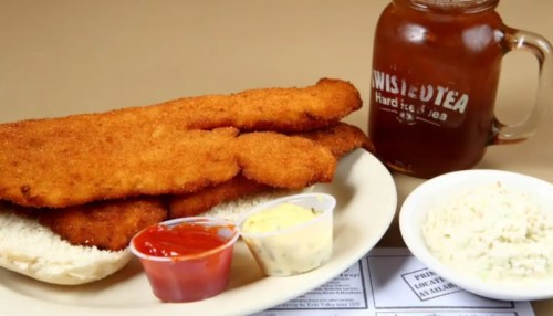 A plate of crispy fried fish fillets with dipping sauces, coleslaw, and a glass of Twisted Tea.
